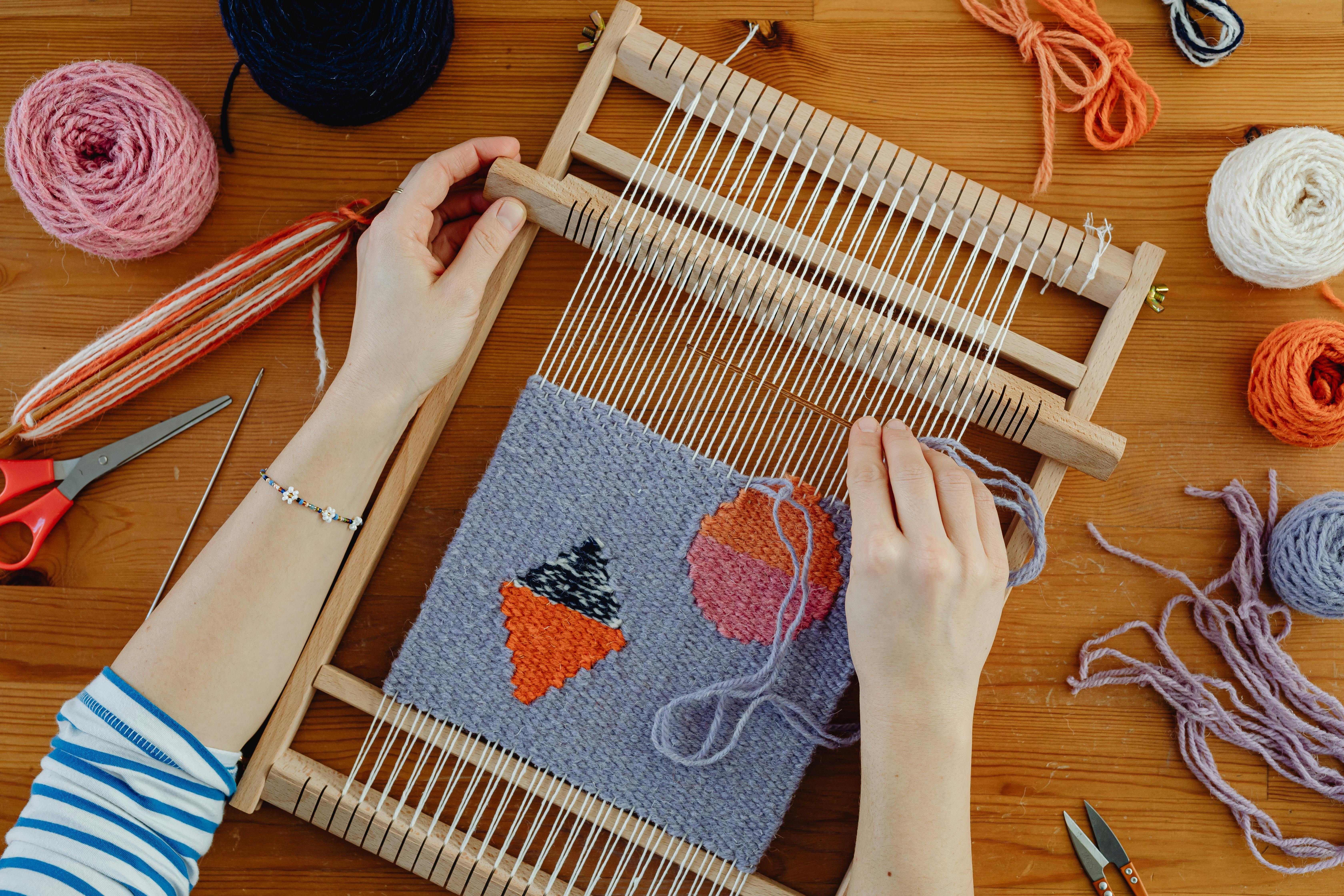 Modern artisan working on small loom with colorful yarn and crafting tools